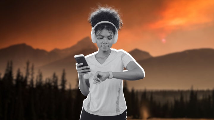 a woman holding her phone and checking her fitness watch. She has headphones over her ears.