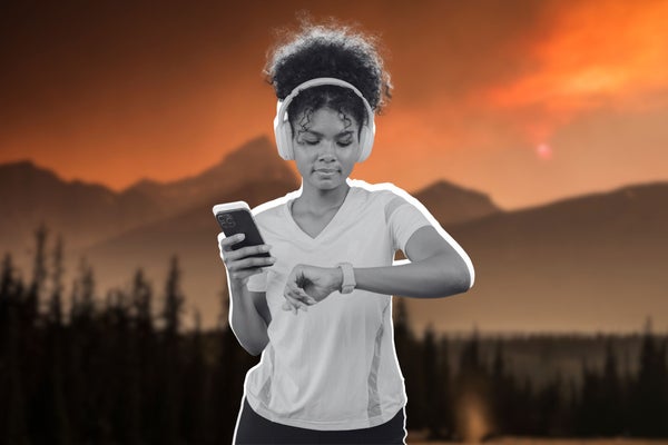 a woman holding her phone and checking her fitness watch. She has headphones over her ears.