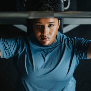 Directly above view of young woman on bench press exercising with barbell at gym