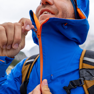A detailed close-up shot of a person zipping up a waterproof blue rain jacket with bright orange lining, highlighting the tech fabric details often discussed in guides on how to wash a rain jacket.