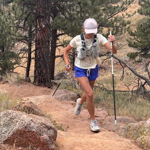 Trail runner testing hydration vest using trekking poles uphill.