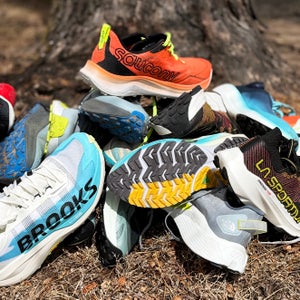 The best trail running shoes for all types of terrain and runners; trail shoes piled up on dirt trail