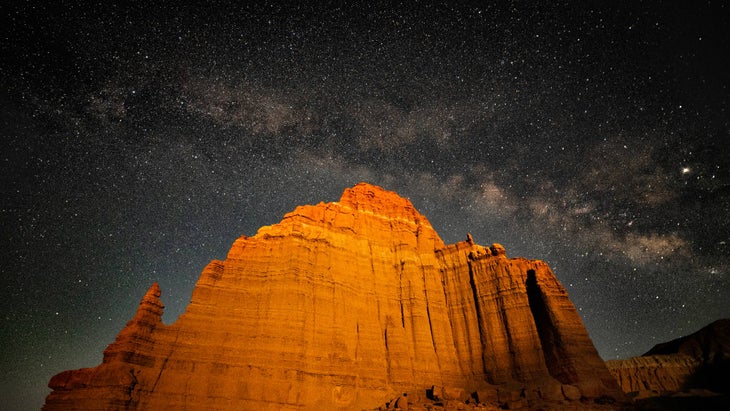 Setting moon lights up face of the Temple of the Moon in Cathedral Valley, Capital Reef National Park, with the Milky Way arcing overhead
