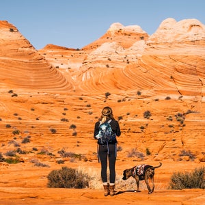 a woman and her dog stand in front of the wave at grand staircase escalante national monument