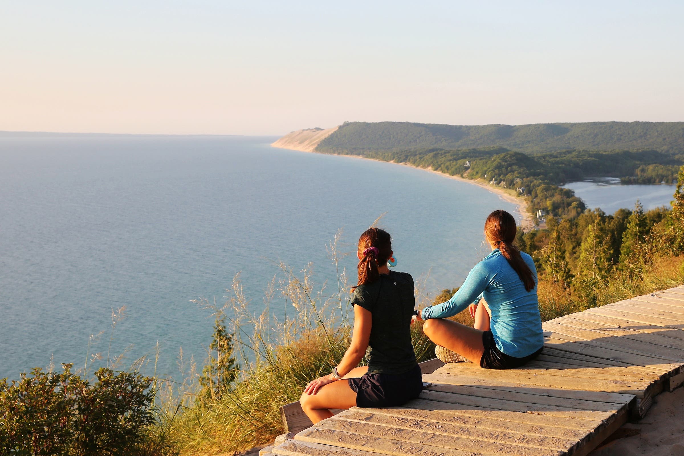 Two women sit on boardwalk at the Empire Bluff Scenic Lookout, overlooking Lake Michigan, the Sleeping Bear Dunes, and the Manitou Island.