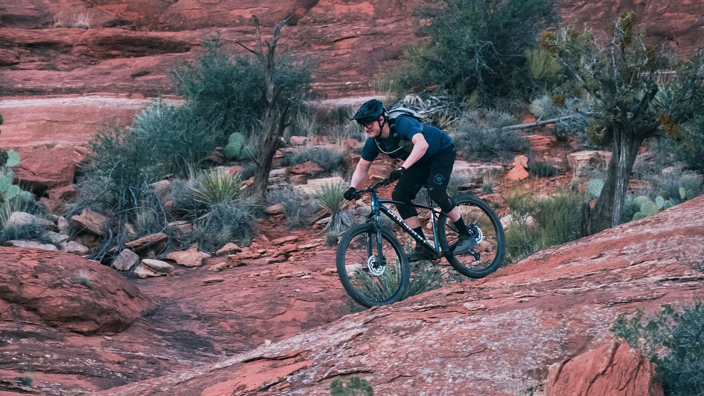 A mountain biker descends a steep red rock slab on a Polygon Xtrada hardtail in Sedona, Arizona