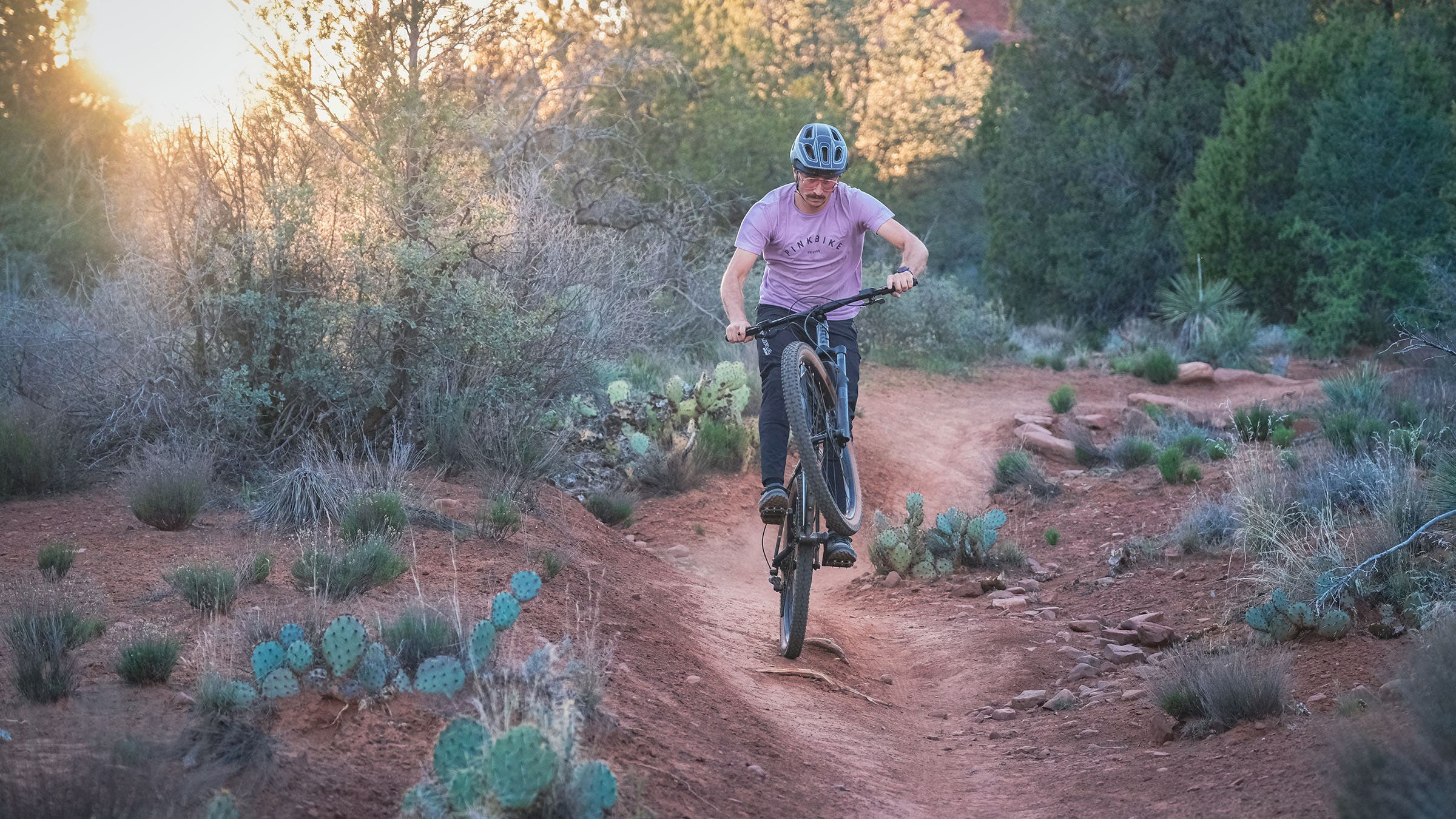 A rider manuals a State mountain bike down a dirt singletrack trail at golden hour in Sedona, Arizona