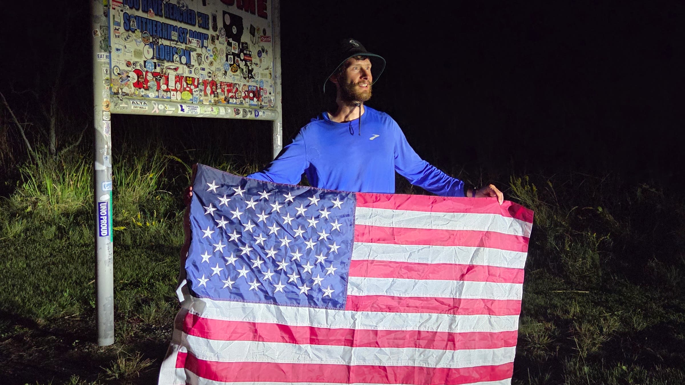 Greg Nance holding a flag in front of a state sign.