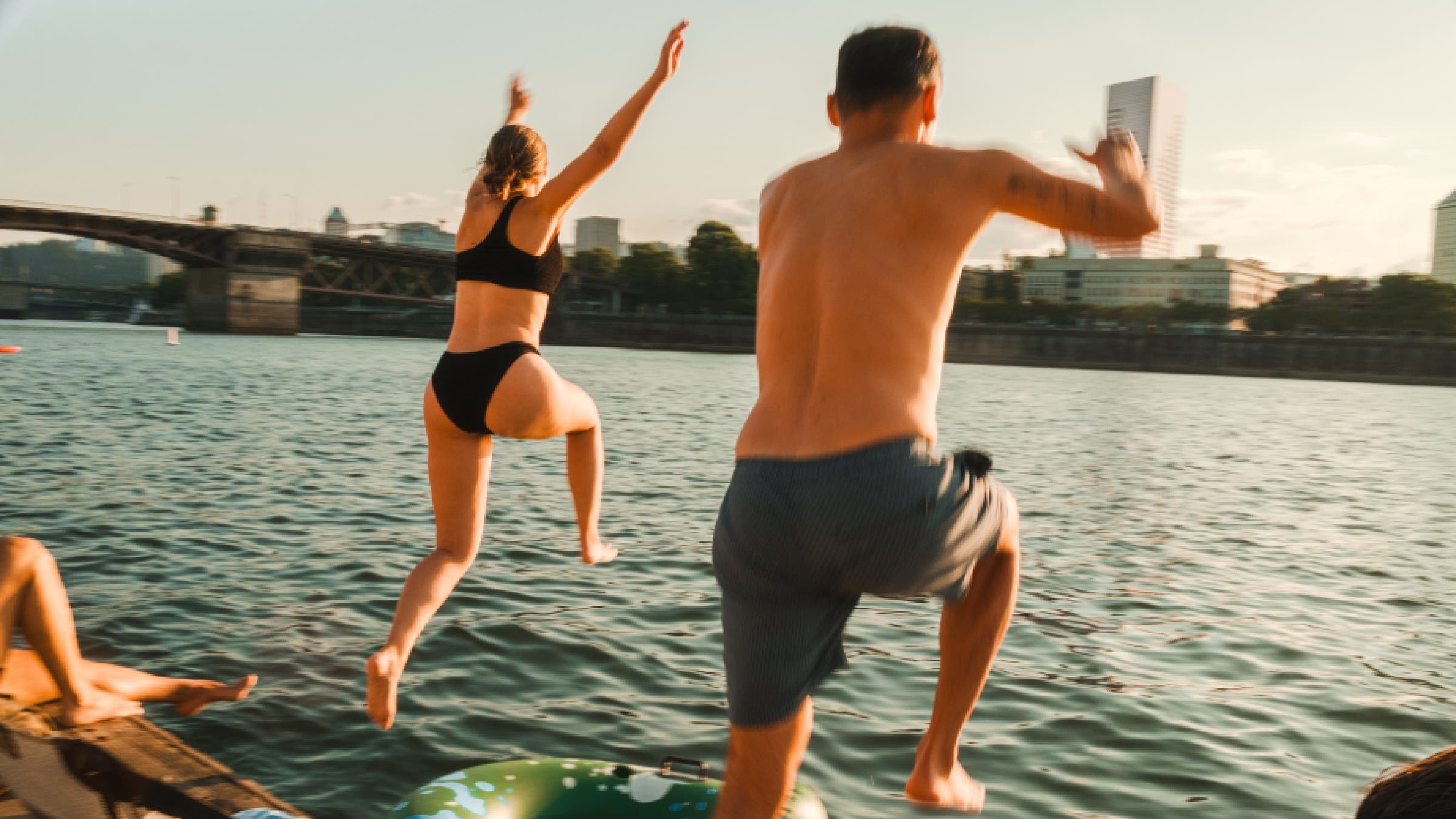 Swimmers jump into a city river.