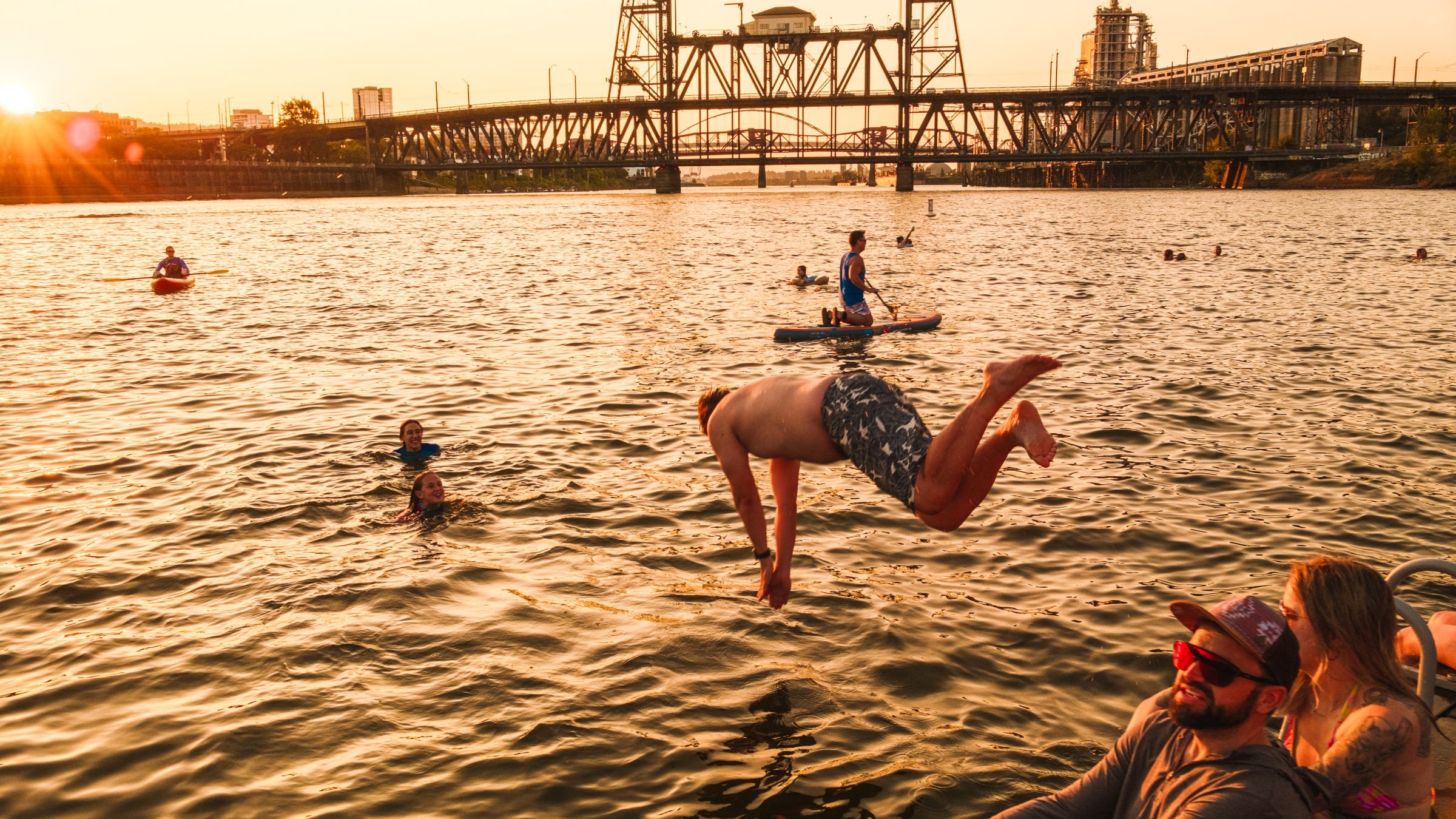A swimmer dives into a large city river at sunset.