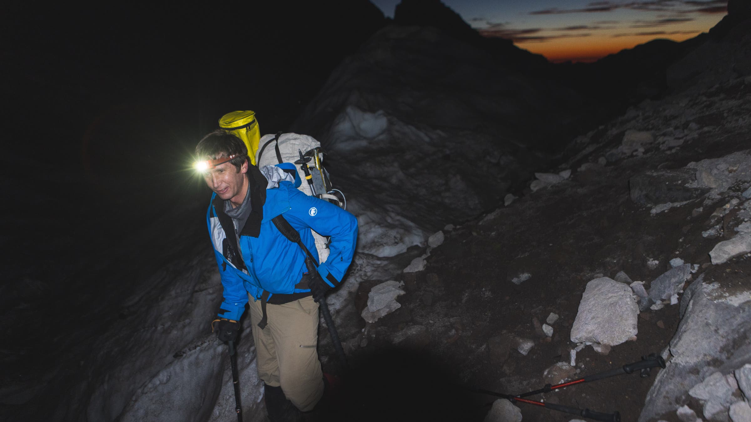 Eric in a headlamp in the mountains with dawn breaking behind him.