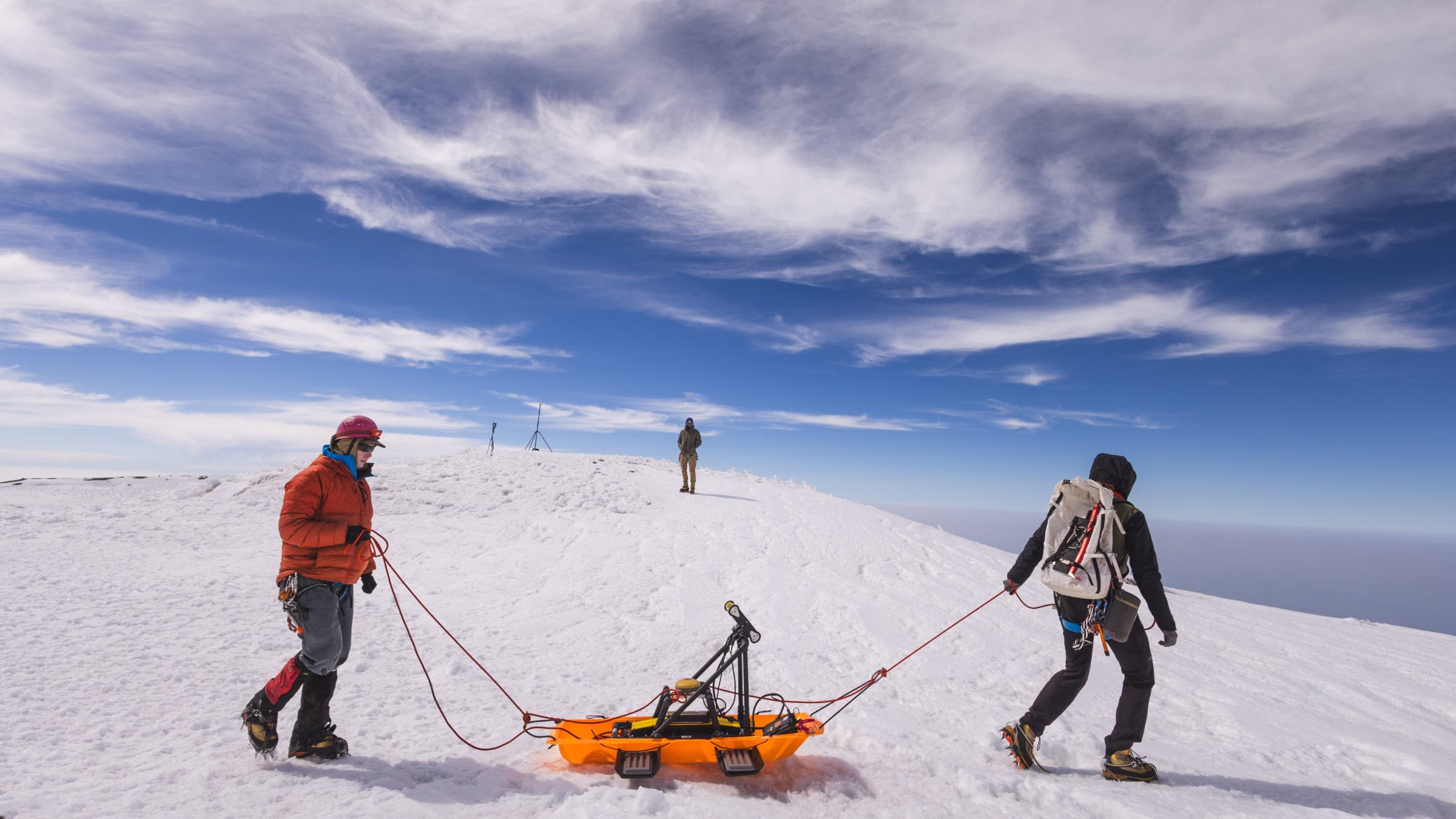 Two people drag measuring equipment in a sled over snow.