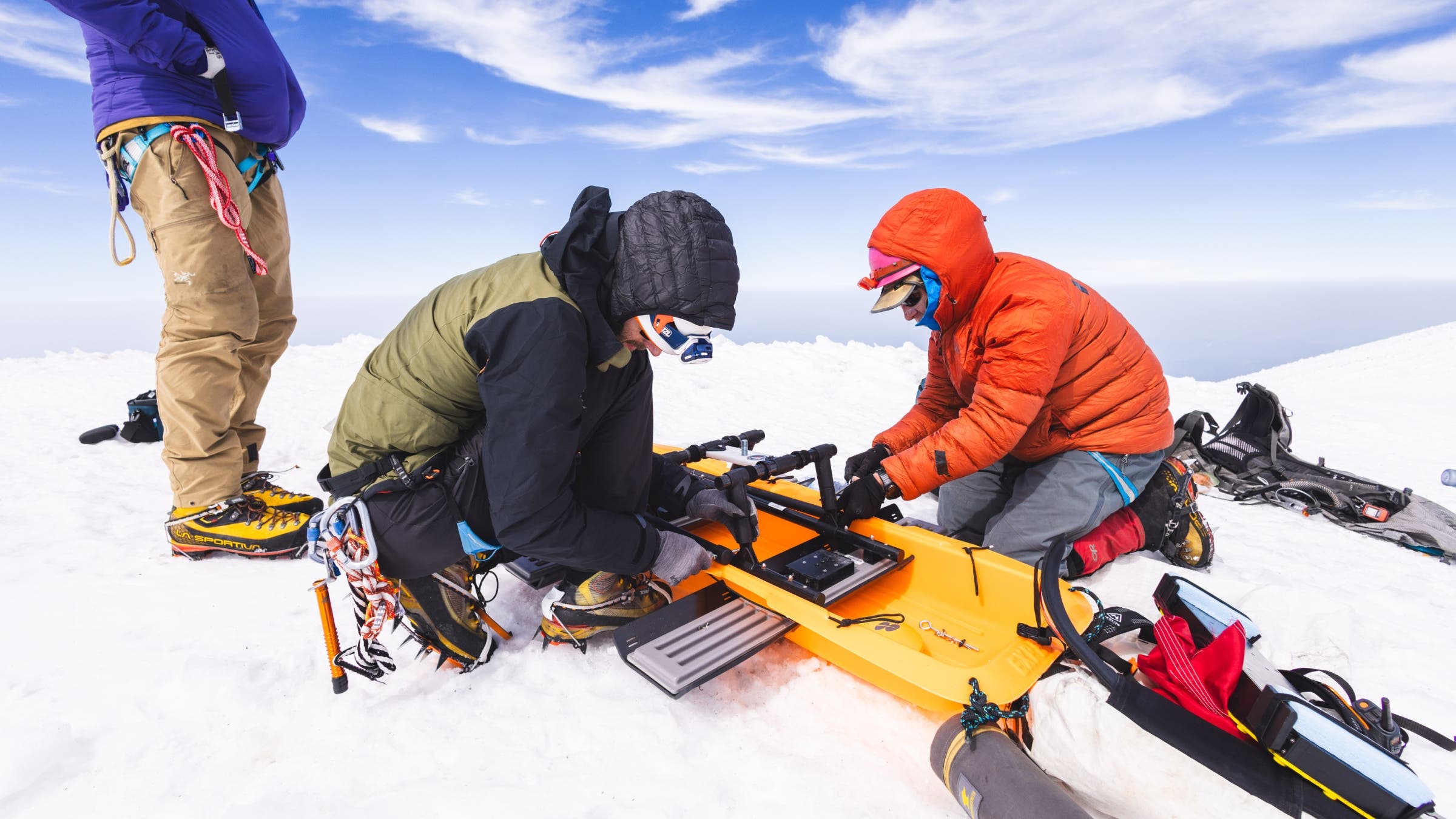 Two people work on equipment in an orange sled.