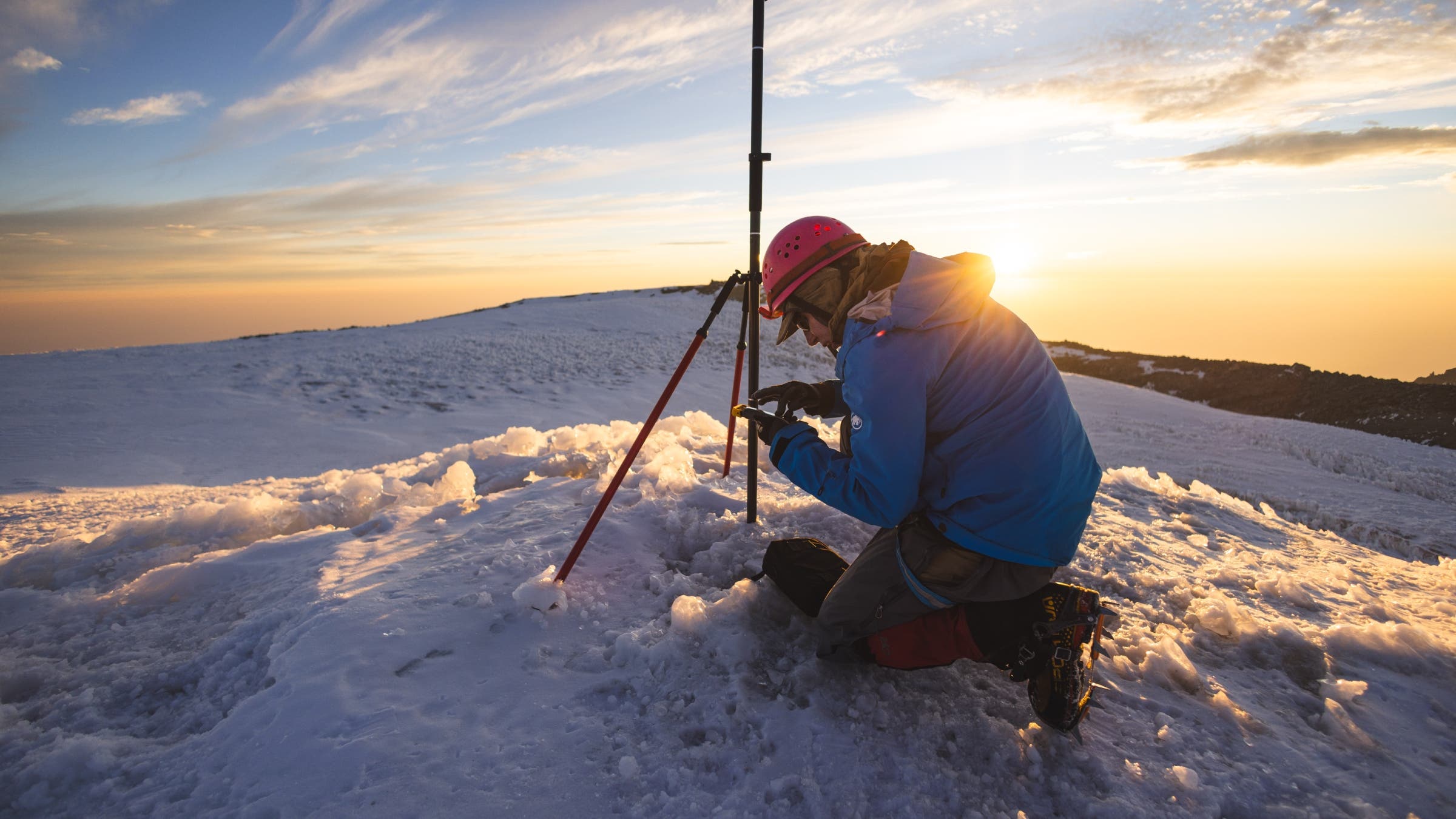 Eric crouching down to look at measuring equipment on a summit at sunset.