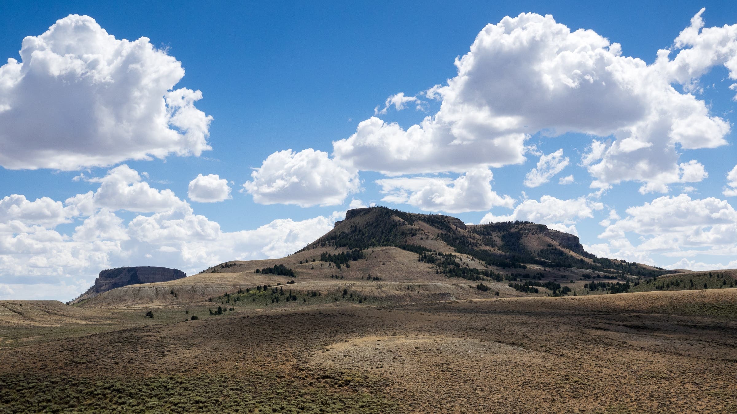 Buttes rising out of a grassy plain on a partly cloudy day.
