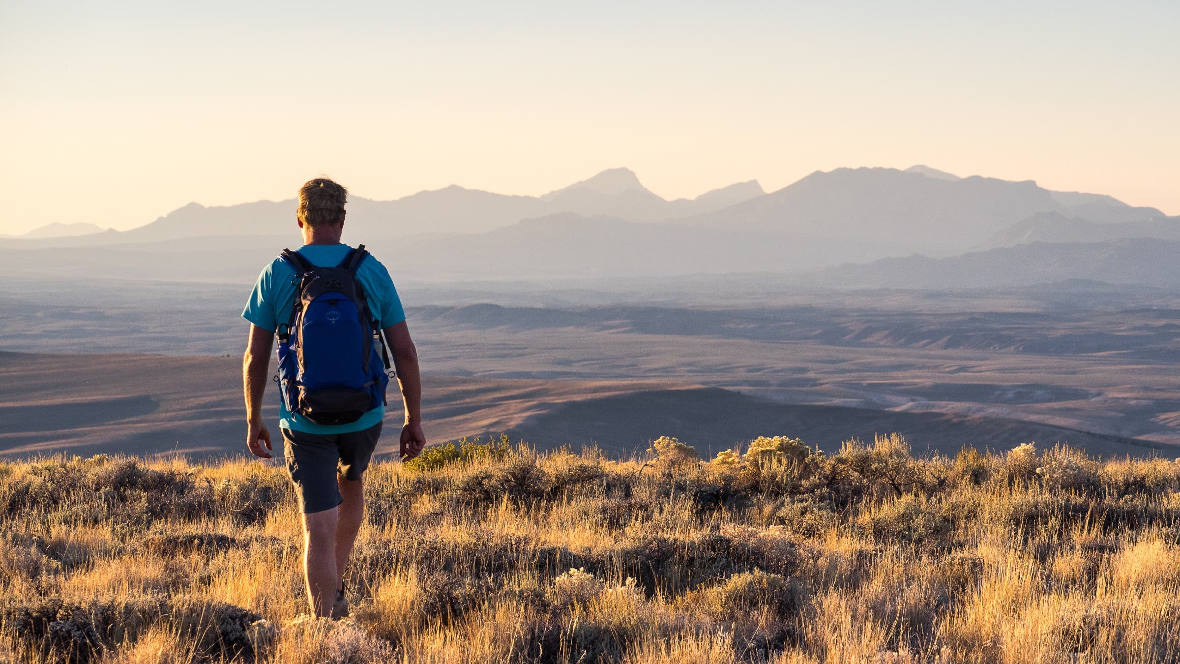 A man walking along a grassy bluff with mountains in the distance.