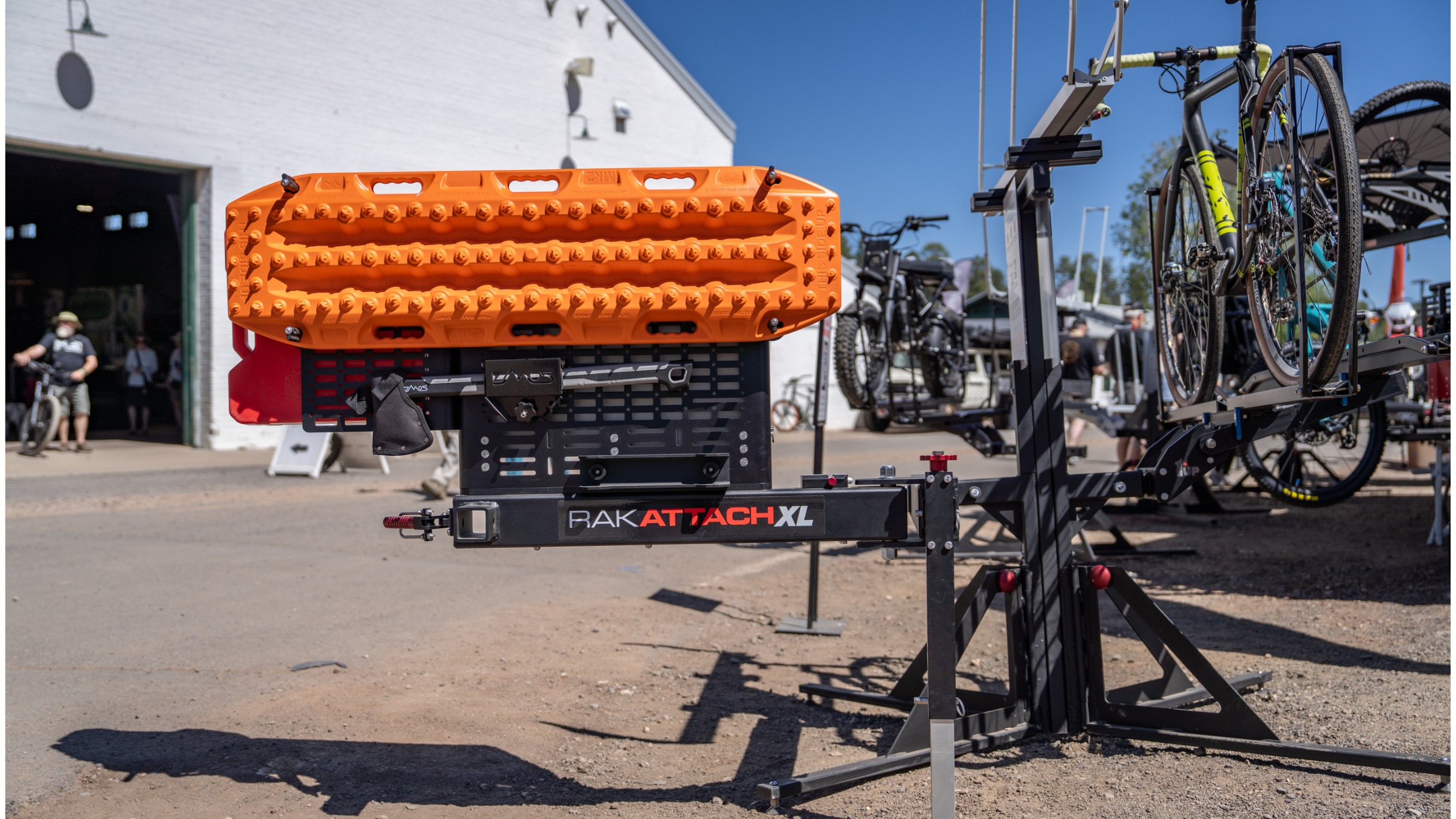 black back of the vehicle storage system sitting on the ground outside at outdoor Overland Expo West with bike loaded and "Rak Attach XL" printed on arm