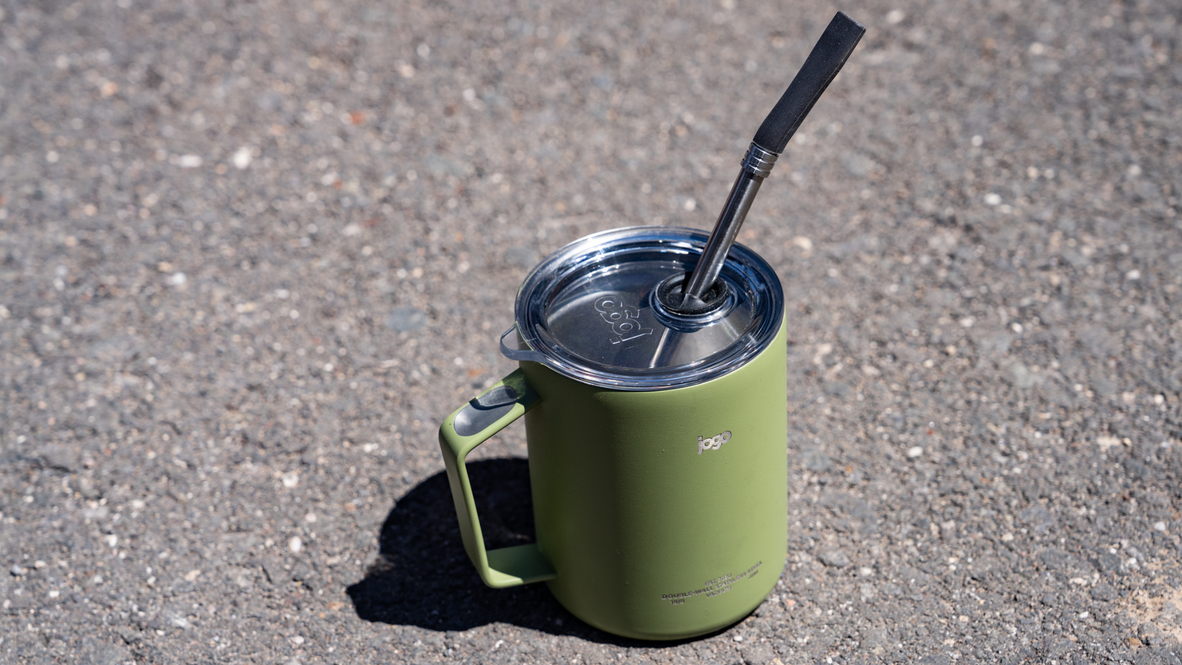 green camping mug with metal straw coming out of it sitting on asphalt outside at 2026 Overland Expo West