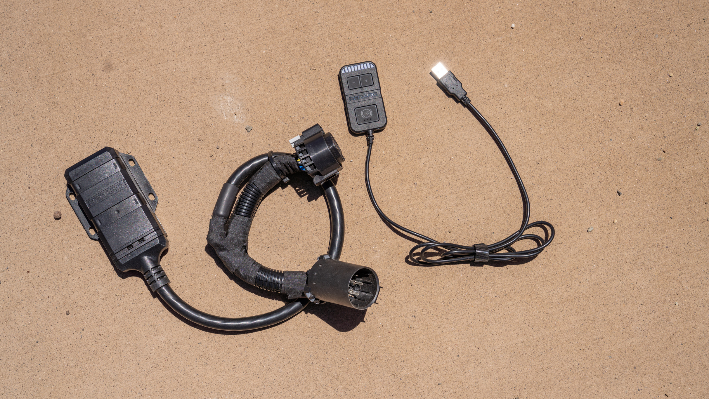 an electric brake controller with black cords on brown dirt outside at Overland Expo West