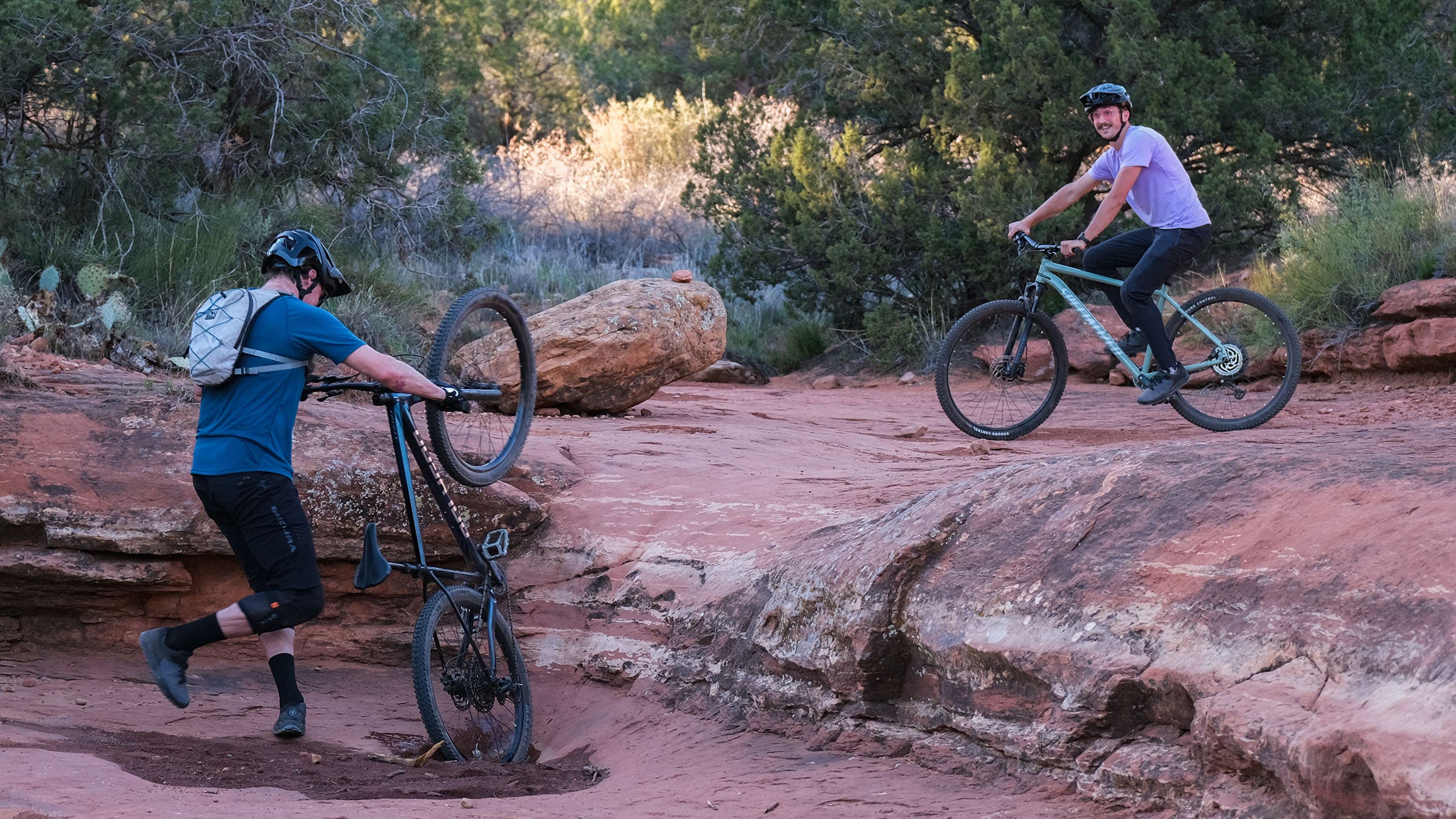 Two mountain bikers on red rock slabs in Sedona, Arizona—one riding smoothly, one mid-crash with his bike flipping over