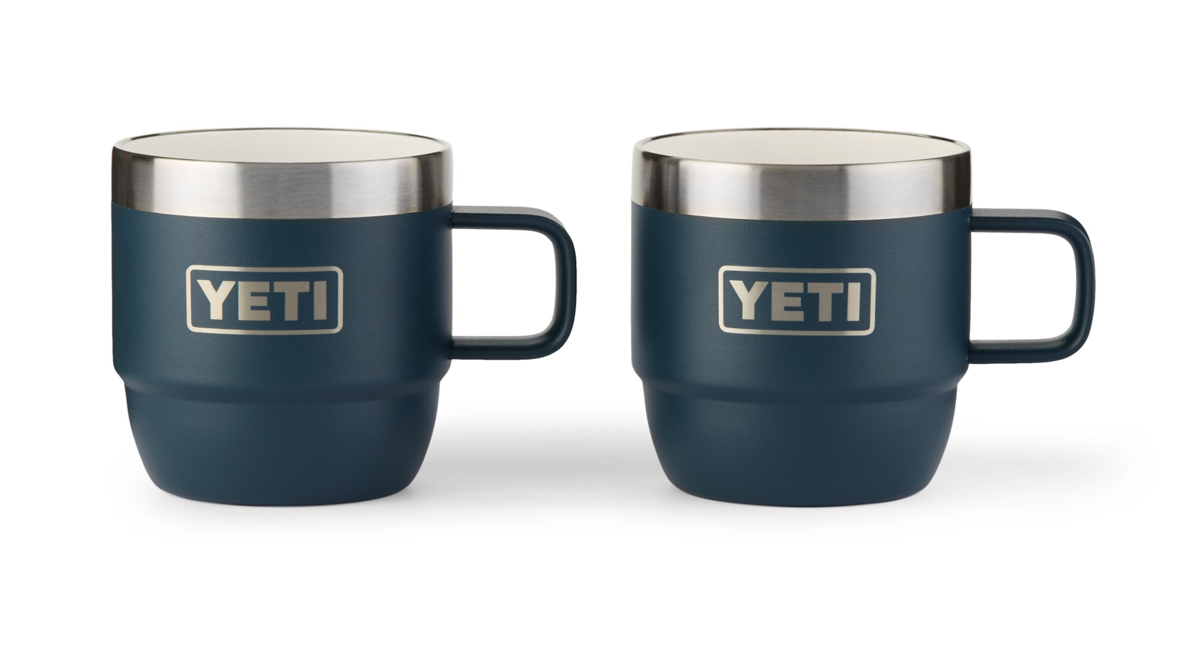 Two navy blue YETI Rambler stackable thermal mugs with stainless steel rims are positioned side-by-side, ready for serving hot camp coffee to outdoor enthusiasts.