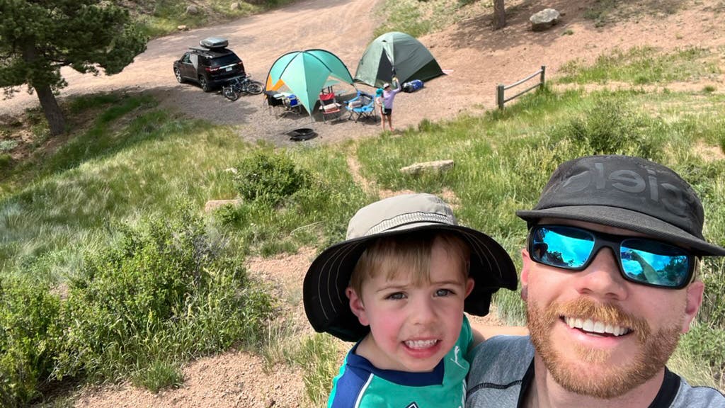 Toddler and dad taking selfie of family camping setup in the background