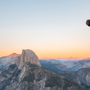 A hiker is standing on an overhanging rock enjoying the view towards famous Half Dome at Glacier Point overlook in beautiful evening twilight, Yosemite National Park, California, USA