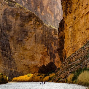 a view of people walking down a shallow river between two canyon walls in big bend national park, texas