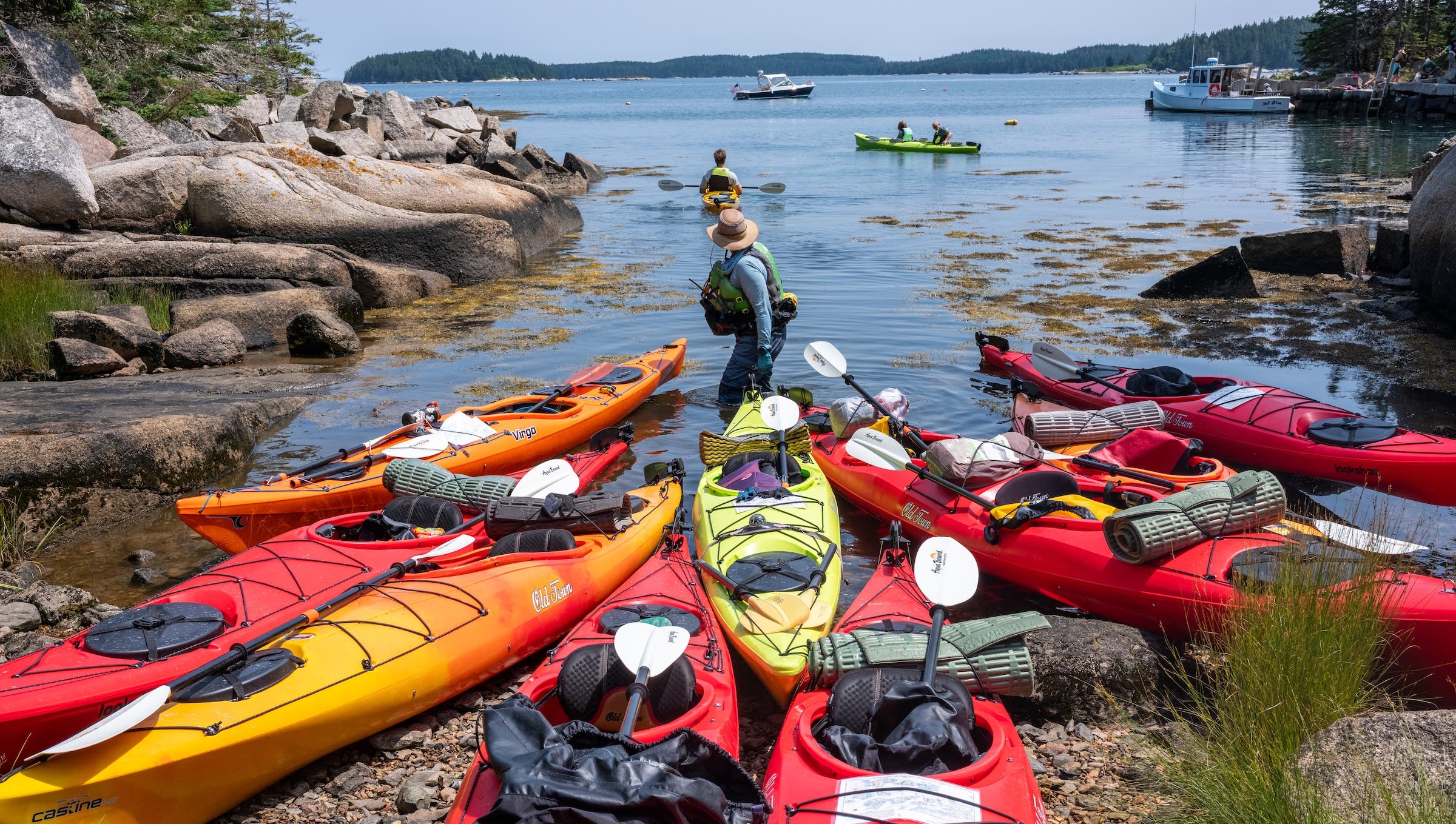 a kayaking guide surrounded by kayaks on the shore at Green Island in Stonington Harbor, Maine in the summer