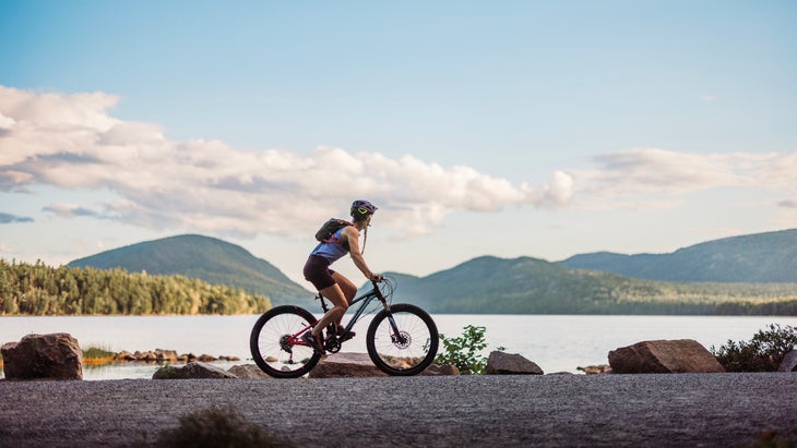 Cyclist rides bike on carriage trail past Eagle Lake, Acadia Park
