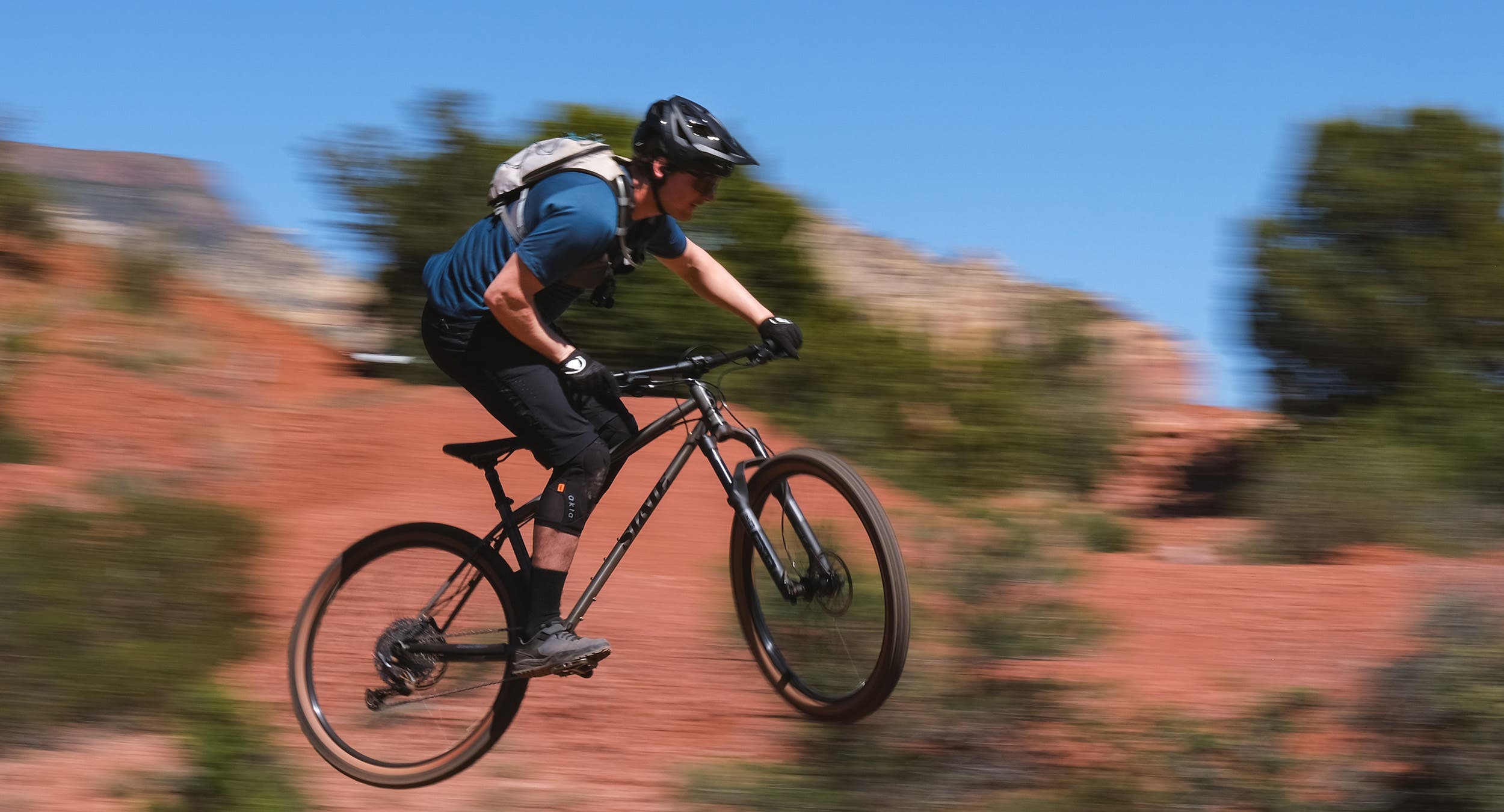 Rider wearing black mountain bike helmet mid-jump on black mountain bike in Sedona, Arizona