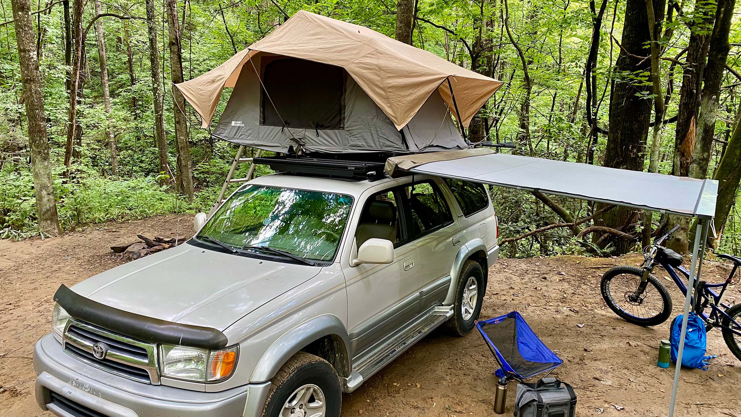 Softshell rooftop tent deployed on Toyota 4Runner at campsite in woods.