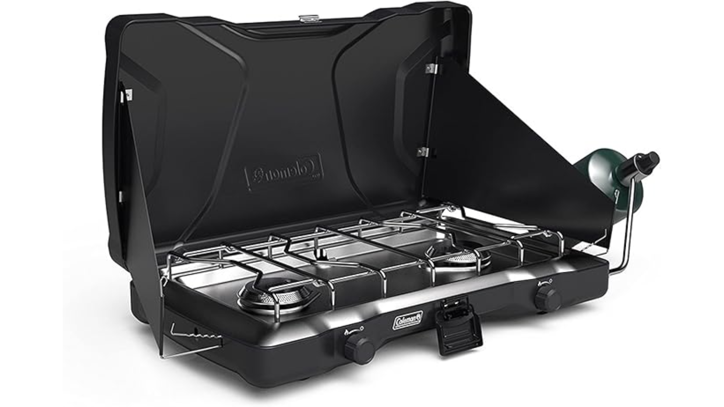 An open, black tabletop Coleman camping stove featuring two burners under a steel grate, built-in side wind guards, and a propane tank regulator attachment on the side.