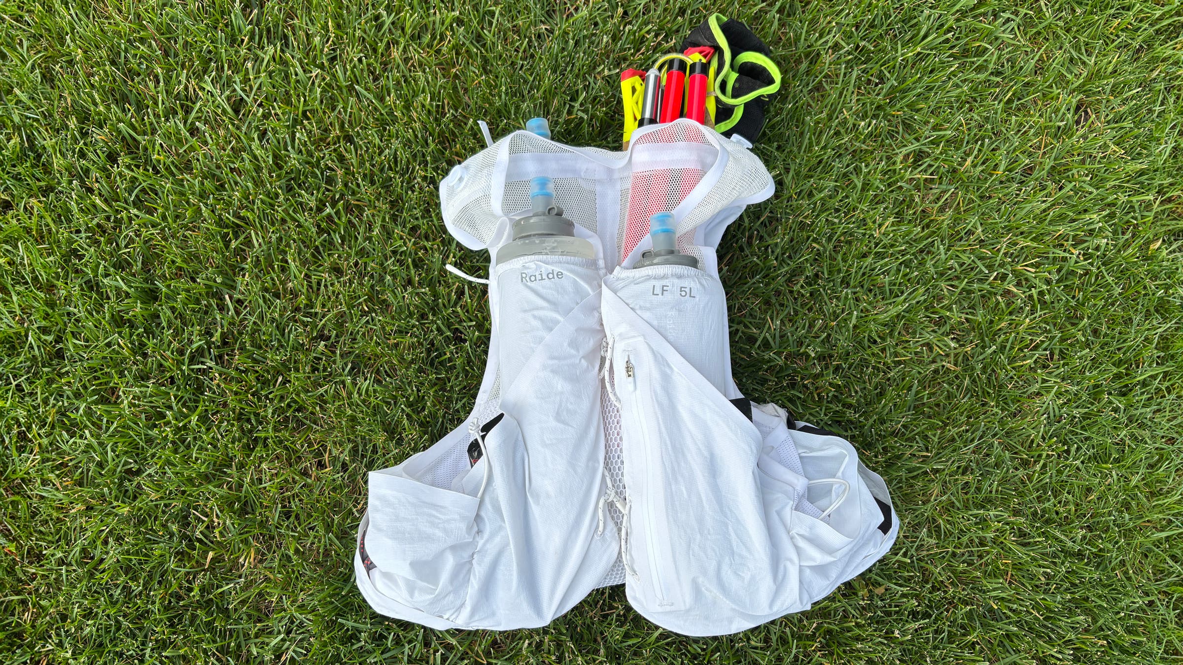 View of front of Raide LF 5L running vest with poles and water bottle in pockets.