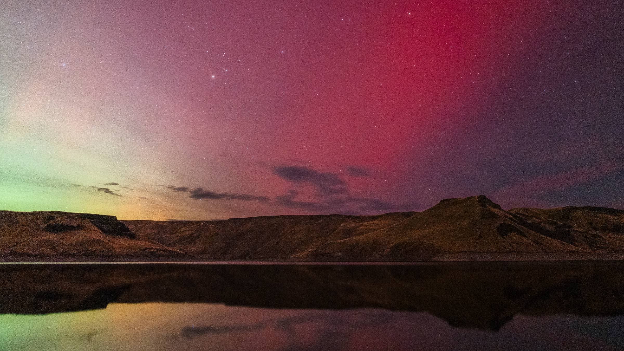 Red and green colors from the Aurora Borealis glow above a lake.