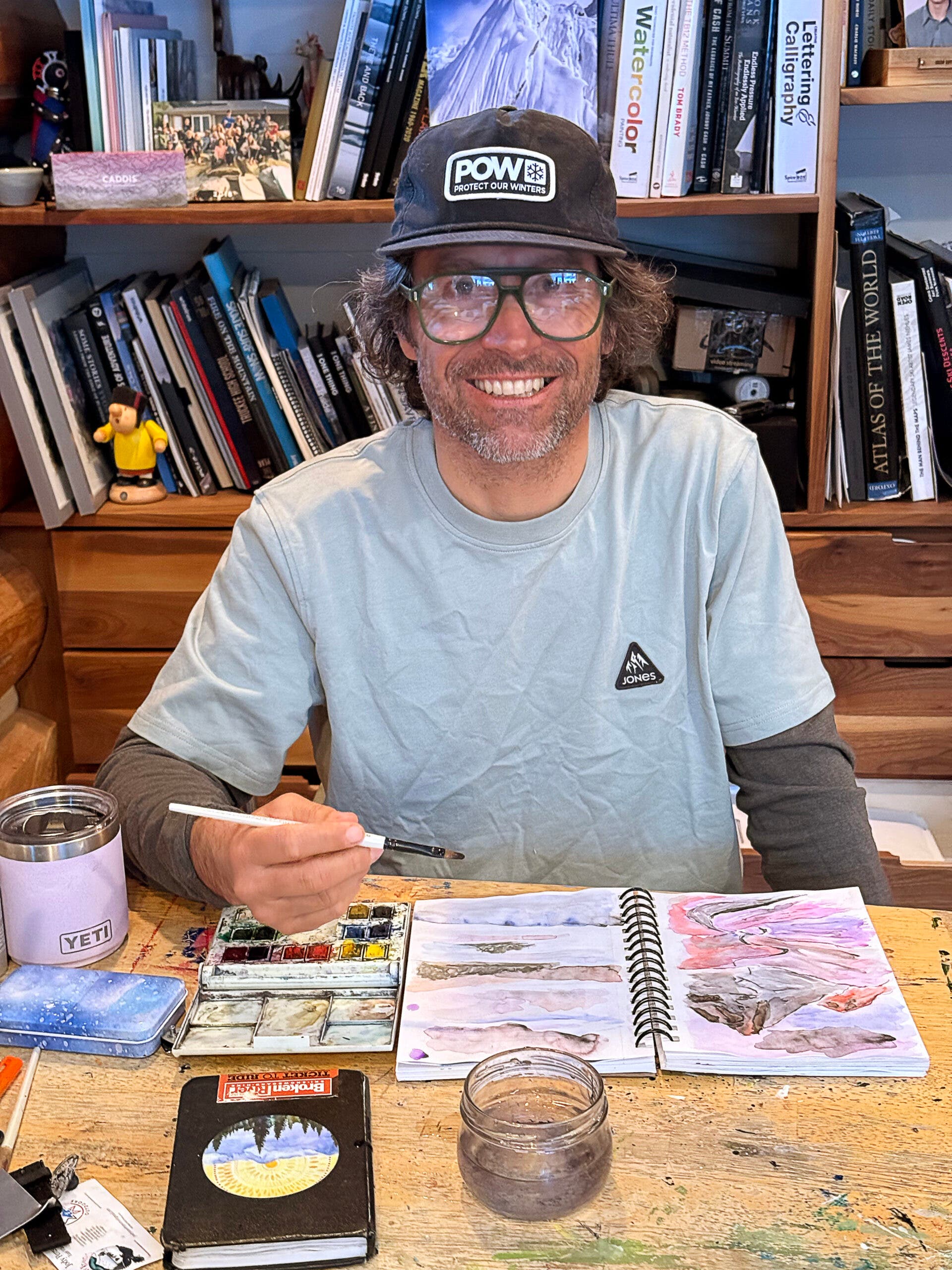 jeremy jones sits at a desk with art supplies while wearing the caddis frames