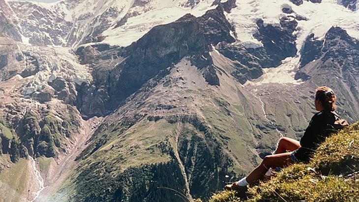 Woman sitting on mountainside enjoying view across a valley to a towering range in the distance