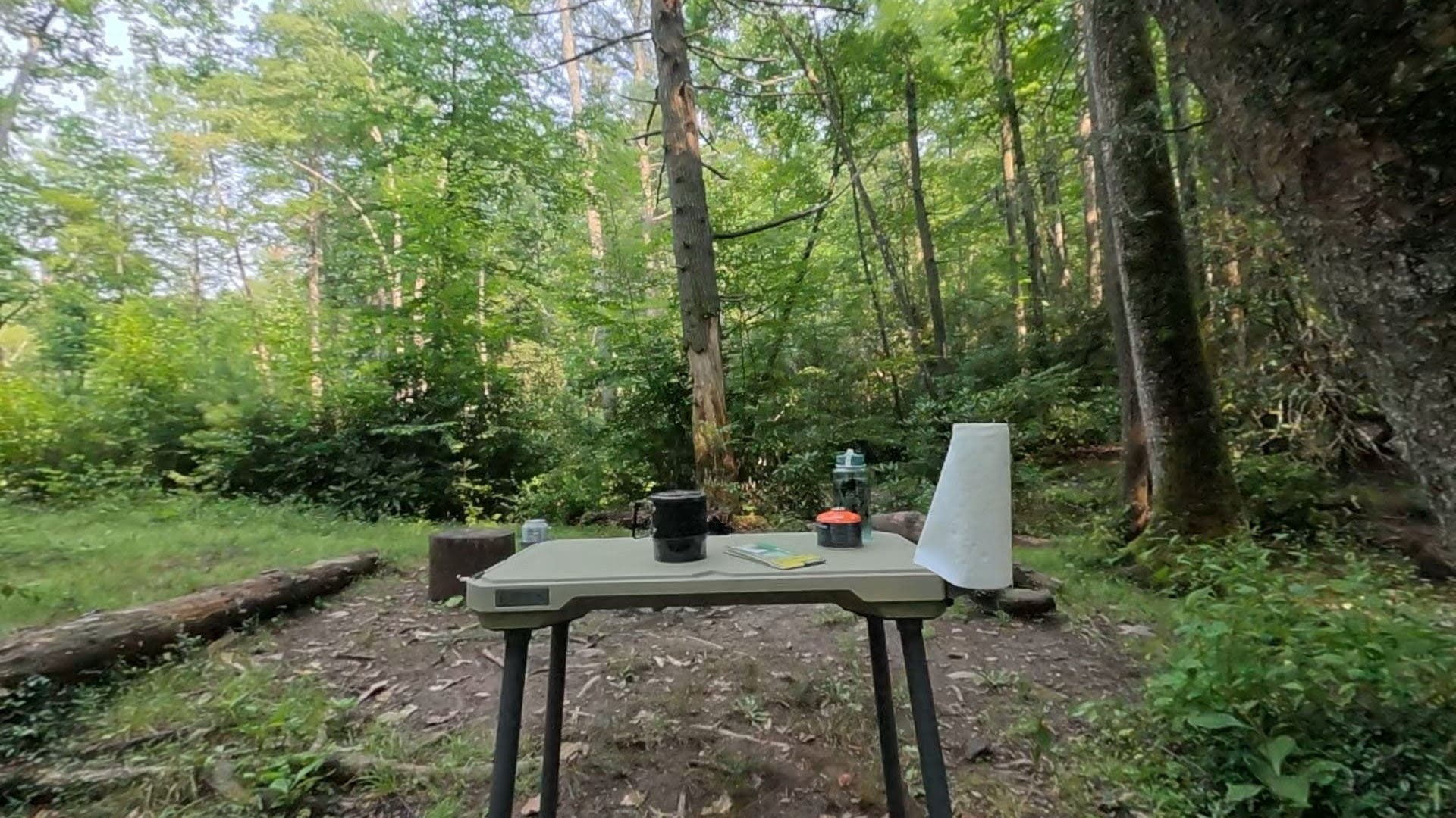 Pecos Outdoor table set up in woods with camp supplies on table surface. 
