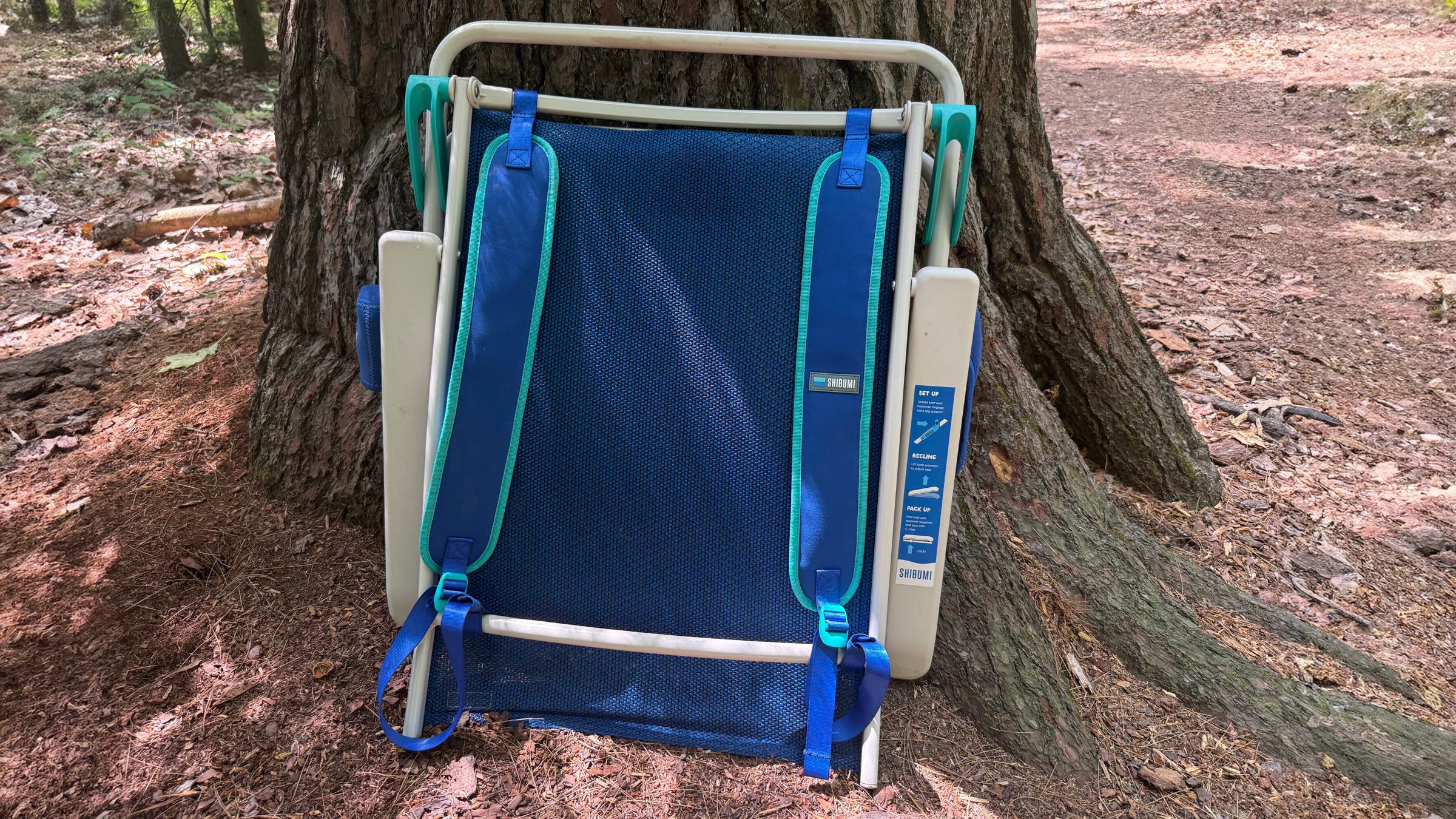 Folded up Shibumi beach chair leaning against a tree for easy transport