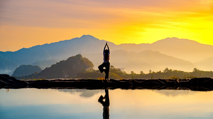 Woman practicing stretching on the high mountain slopes in the morning mist and by the reflection ponds