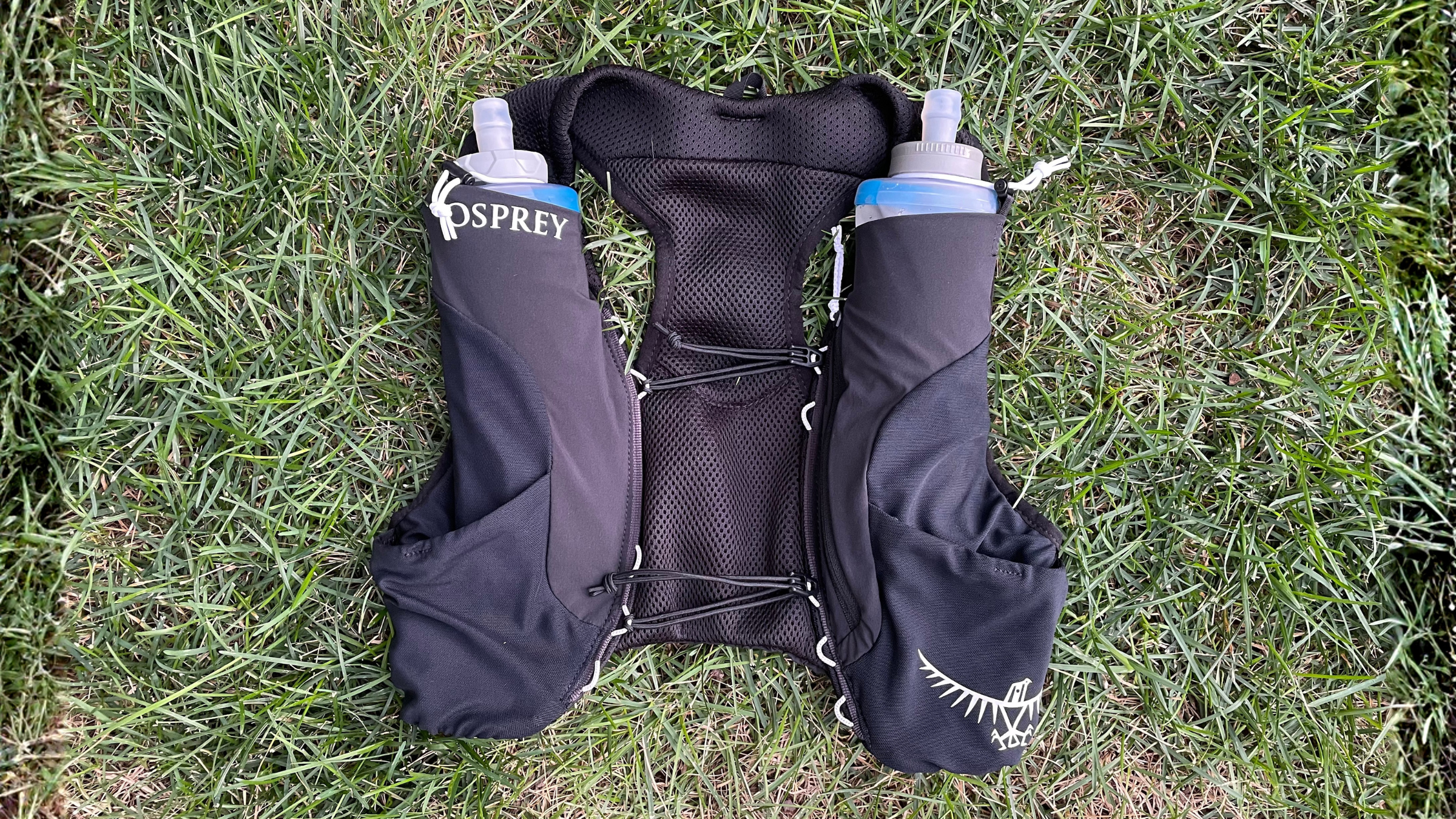 Black Osprey trail running hydration vest featuring front water bottle pockets displayed flat on a lawn.