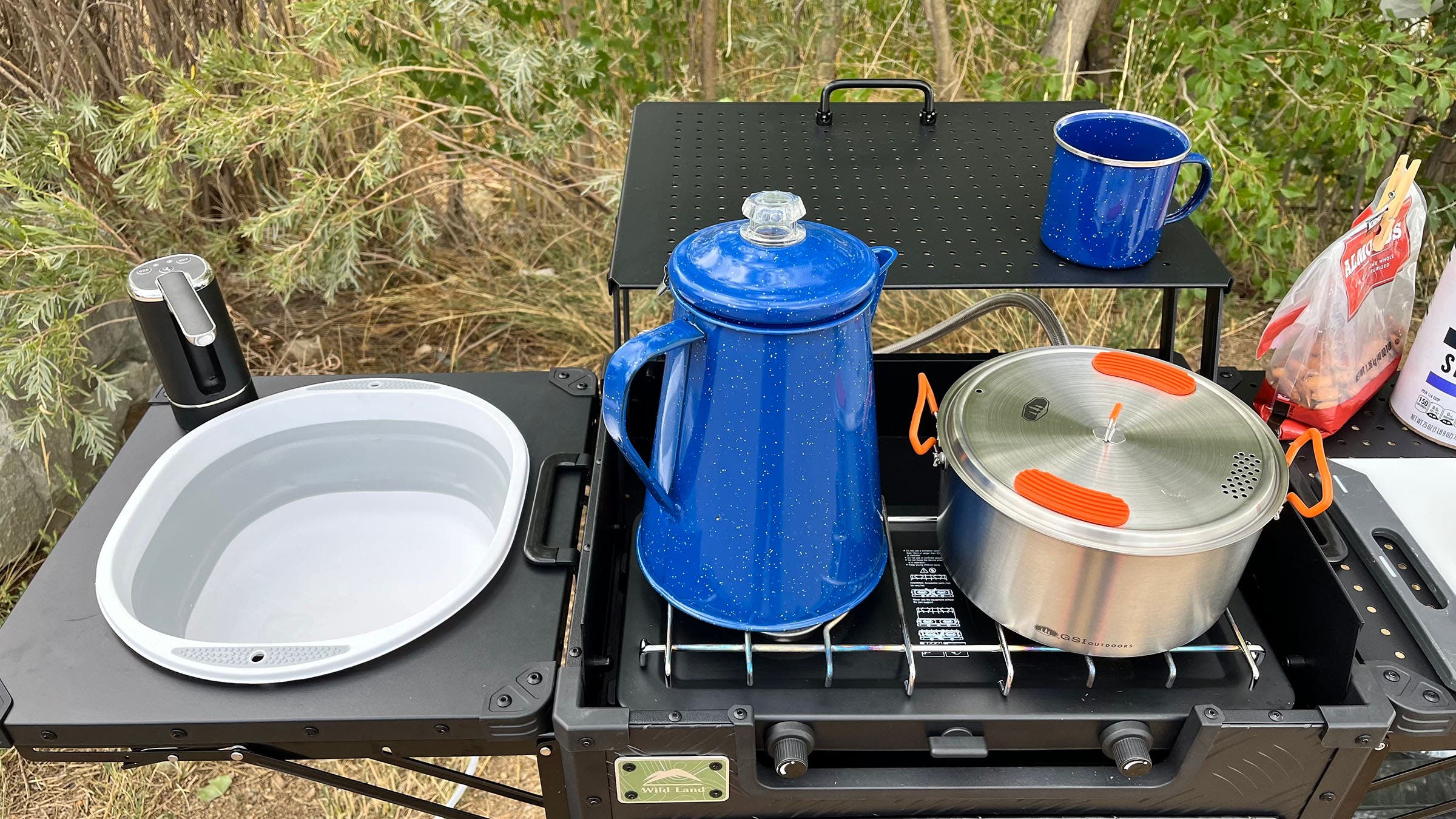 Close-up of the Cinch Kitchen Cruiser's stove with a percolator and pot cooking, a collapsible sink to the left, and a mug on the small overhead shelf.