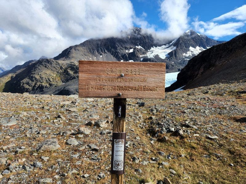 a sign marking crow pass is shown against a mountainous background