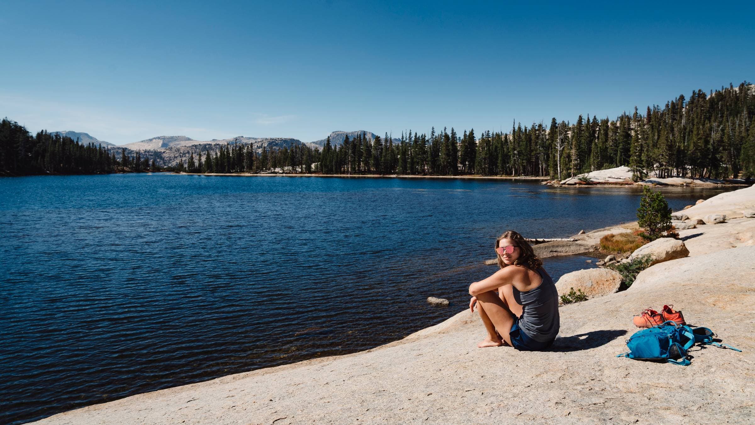 A woman rests from a hike on the shore of Cathedral lake.