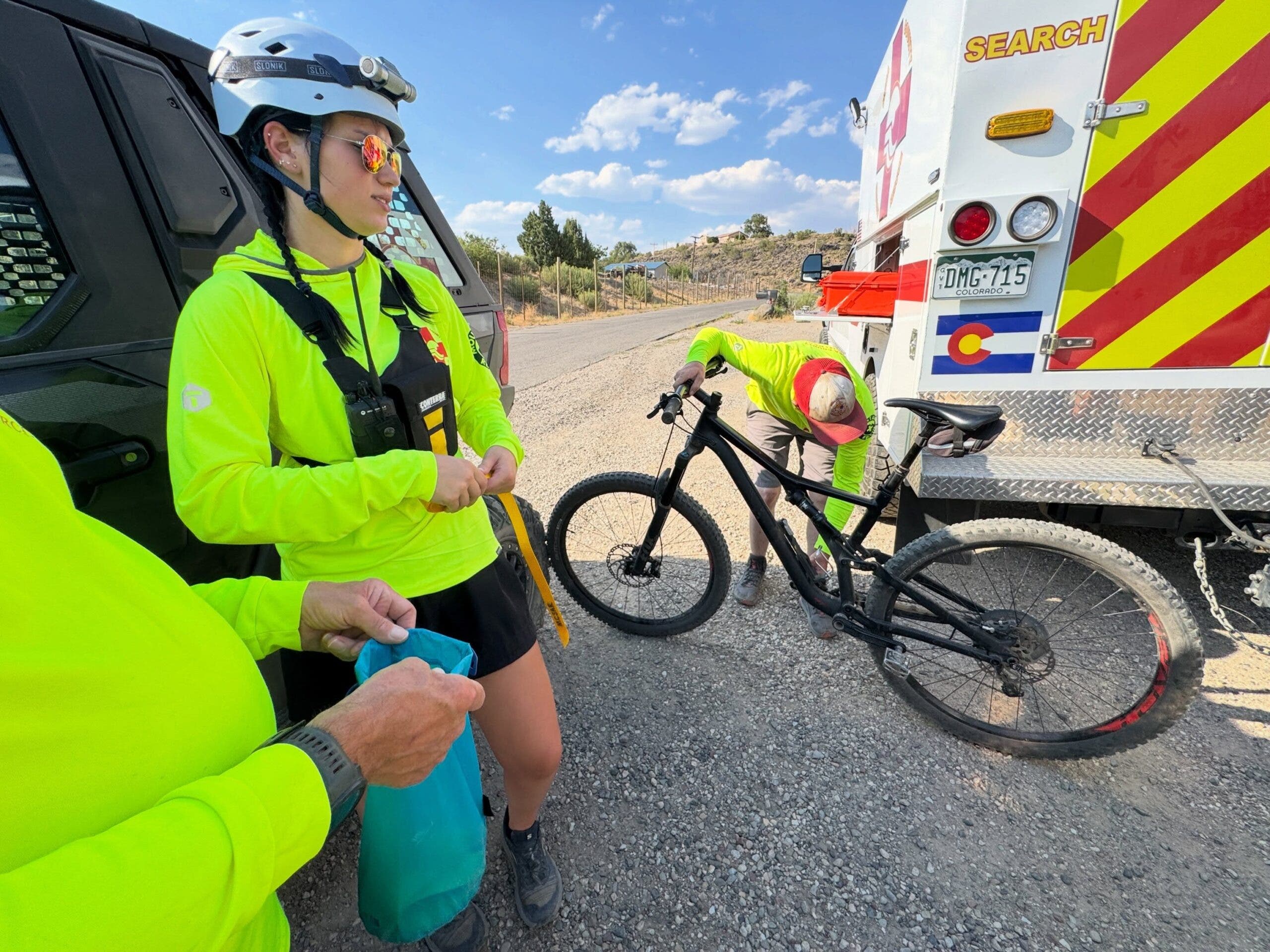 search and rescue crews wearing neon shirts next to a mountain bike and ambulance