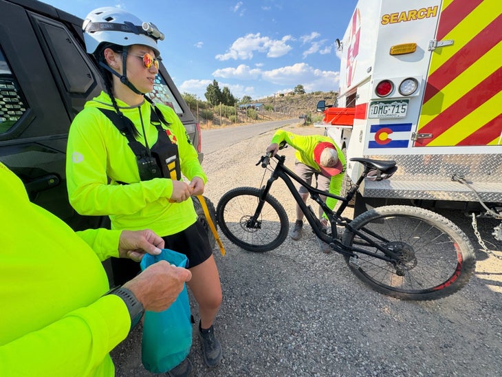 search and rescue crews wearing neon shirts next to a mountain bike and ambulance