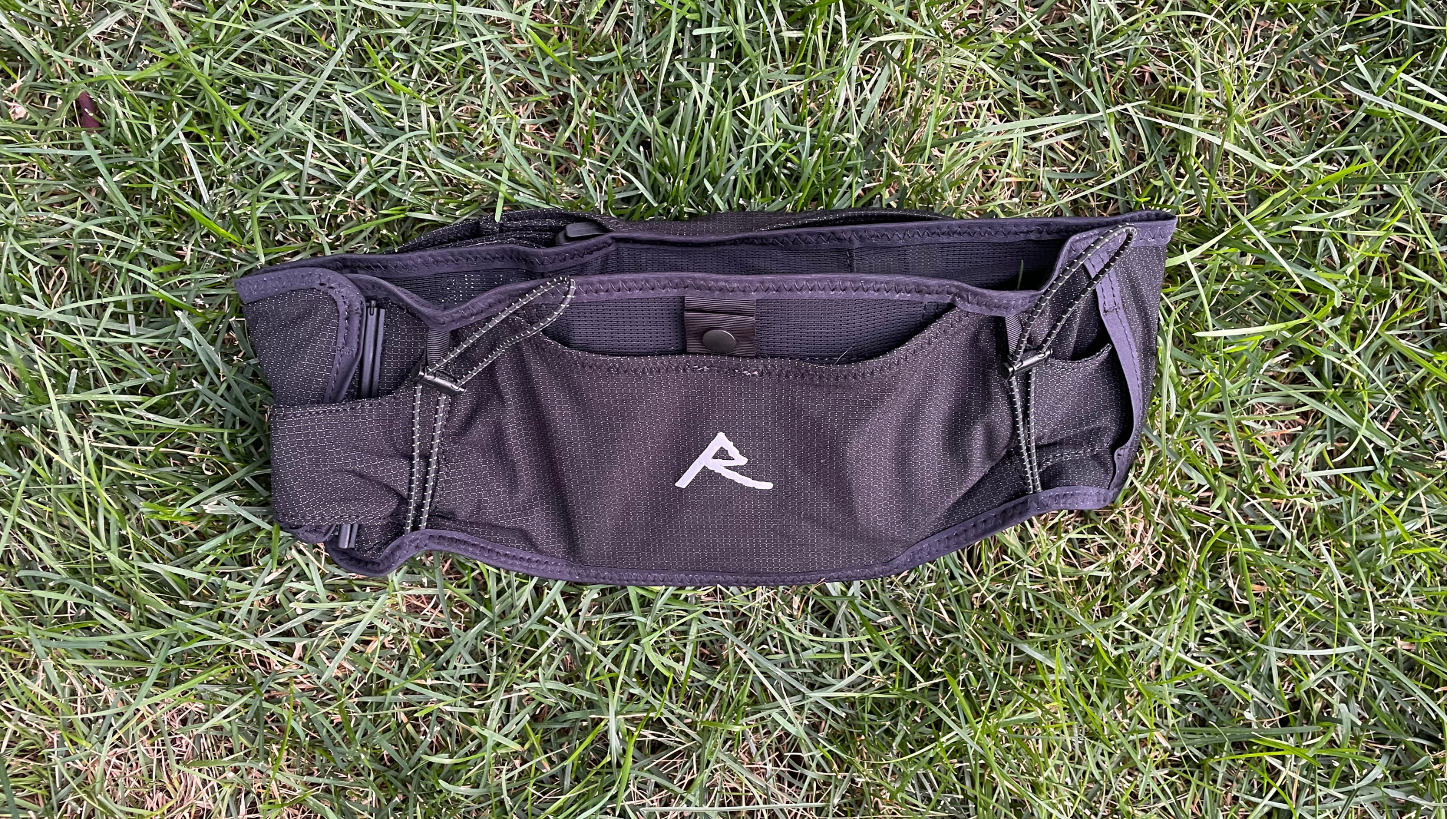 Black Raide trail running waist belt with a white central logo laid flat on green grass.