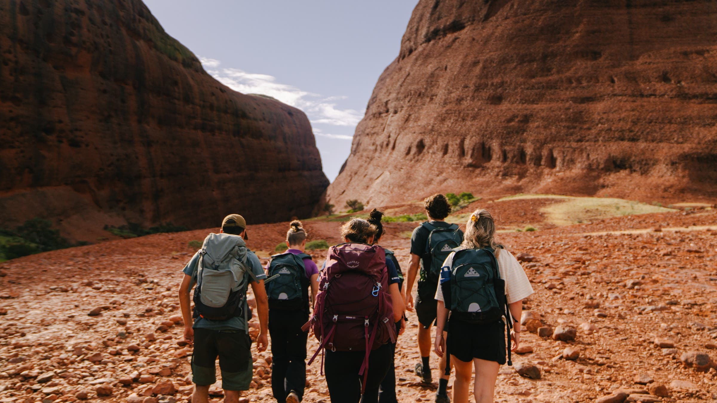 A group of hikers walks through a red-rock gully.