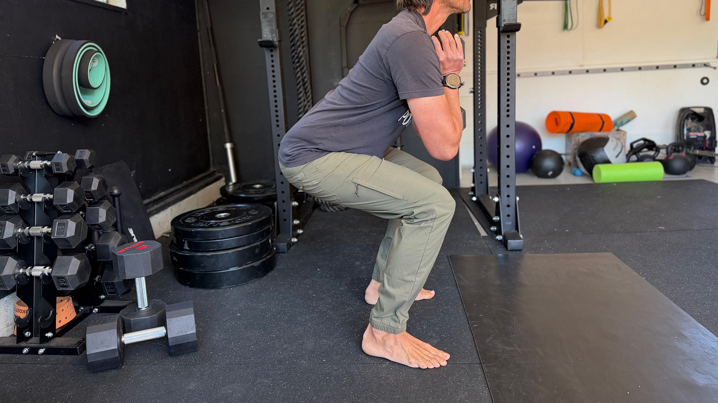 Lower half of man performing exercise squat in gym wearing joggers