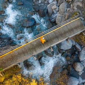 An overhead aerial/drone view of an unrecognisable person walking over a bridge that crosses a beautiful mountain stream in the French Alps - stock photo